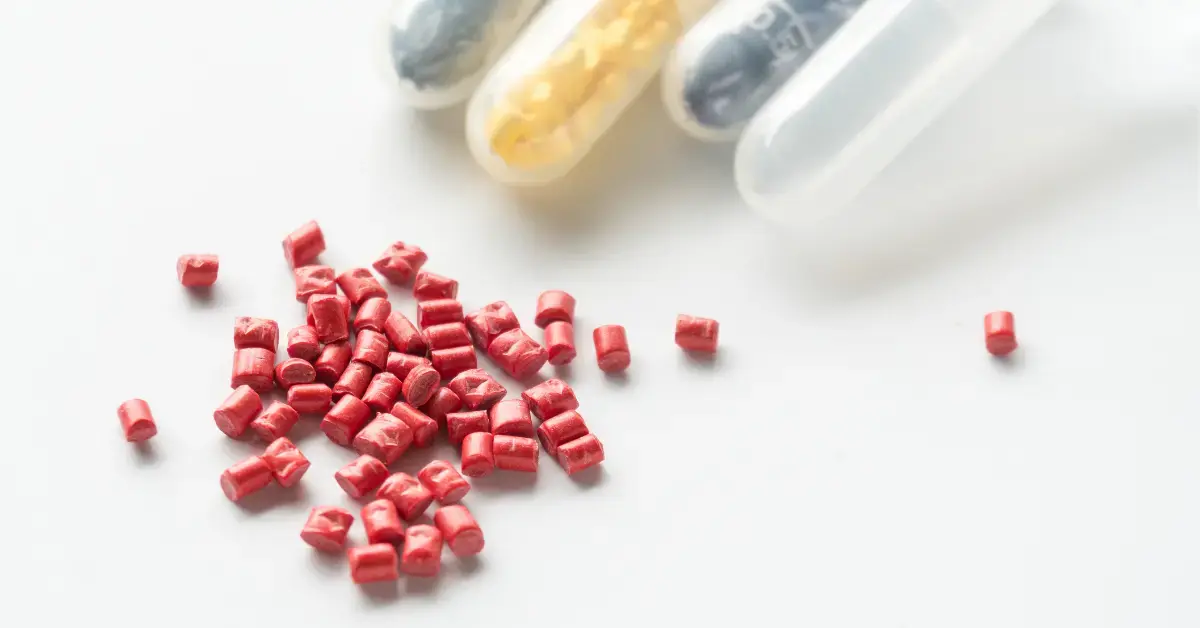 Rotes Kunststoffgranulat für Medical-Grade-Materialien vor Reagenzgläsern mit Proben auf weißem Untergrund