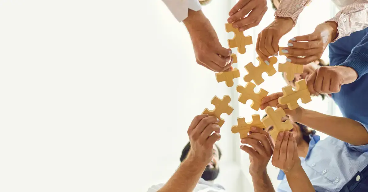 Teammitglieder arbeiten zusammen, indem sie Puzzleteile zusammensetzen – ein Symbol für funktionsübergreifende Teamarbeit, strategische Partnerschaft und erfolgreiche Projektintegration in einem professionellen Geschäftsumfeld.