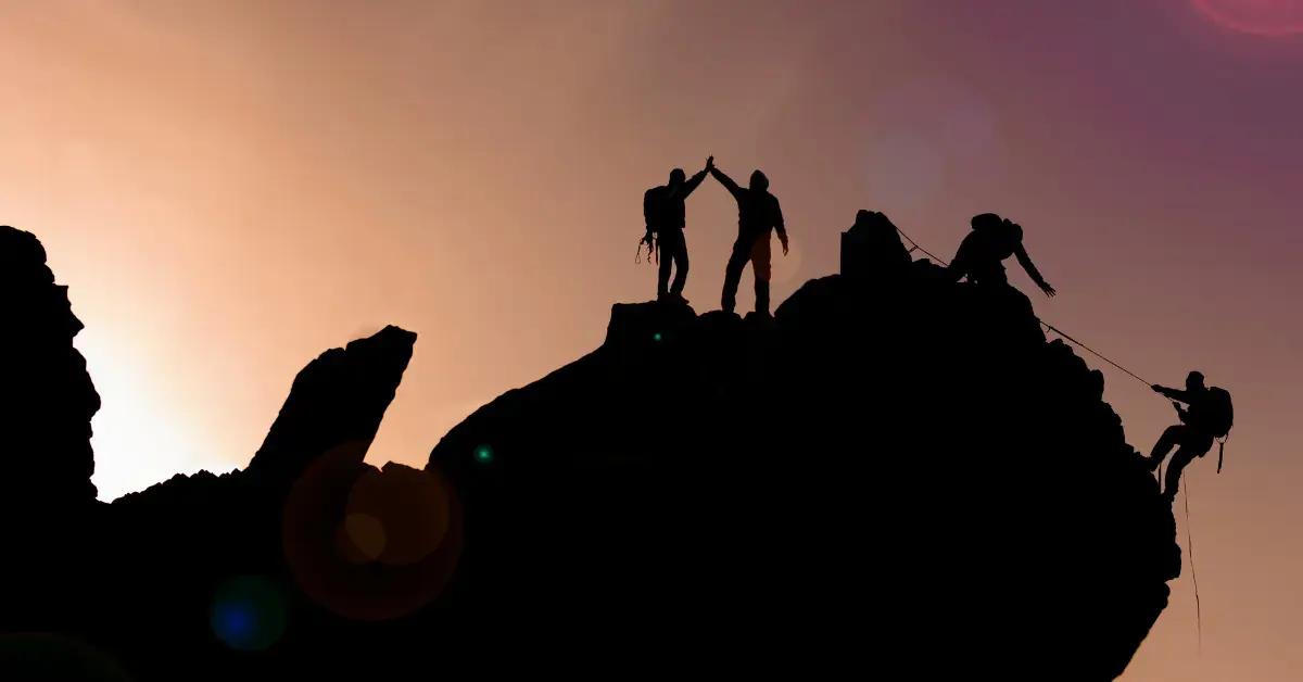 Bergsteiger unterstützen sich gegenseitig beim Erreichen eines Gipfels – Symbol für erfolgreiches Change Management und Teamarbeit im Qualitätsmanagement der Medizintechnik.